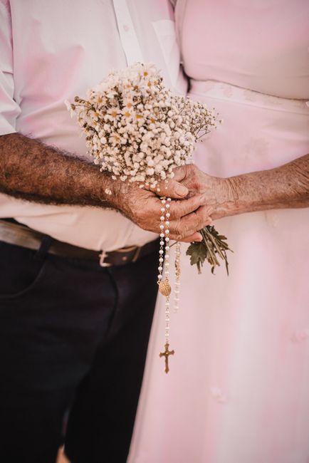 A close-up of a bride and groom holding a delicate bouquet of small white baby's breath flowers, wrapped with green foliage at the stems. The bouquet is casual yet elegant, emphasizing the freshness a